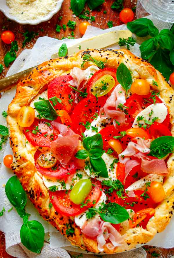 Lekker makkelijk recept voor Caprese plaattaart, een veelzijdig zomers gerecht voor op je weekmenu. Krokant bladerdeeg met pesto crème, tomaat, mozzarella en eventueel wat gedroogde ham. Eenvoudig vegetarisch te maken en klaar in amper 30min. Je kan dit ook als hapje of voorgerecht serveren