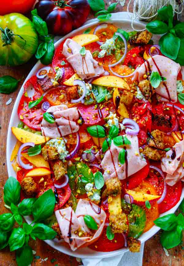 Lekker makkelijk recept voor Tomaten salade met pesto, simpel snelle salade voor bij een BBQ - barbecue of als doordeweekse maaltijd. Fris, licht, zomers en gezond. Dunne plakjes tomaat, perzik, pesto ricotta crème, pesto croutons en mortadella. Heerlijke dagelijkse kost
