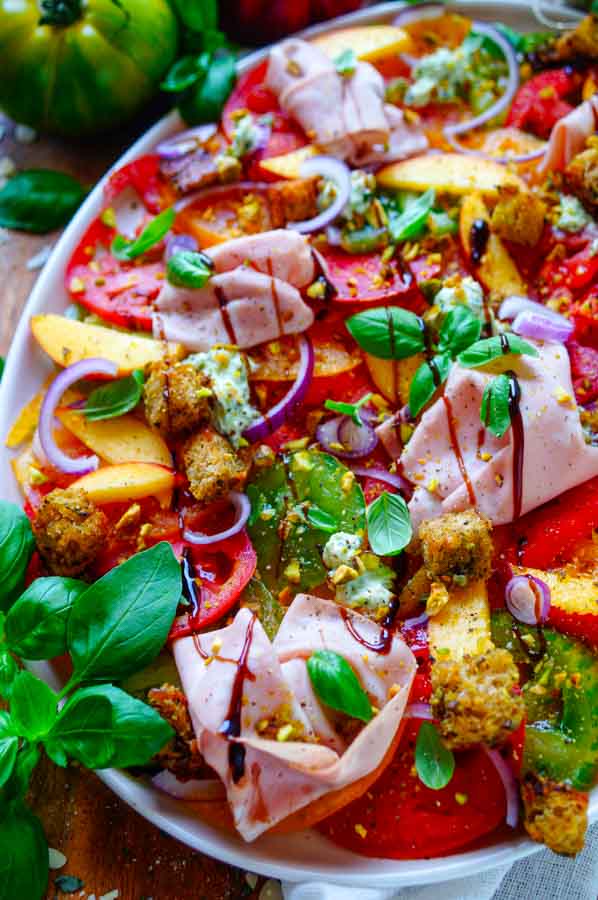 Lekker makkelijk recept voor Tomaten salade met pesto, simpel snelle salade voor bij een BBQ - barbecue of als doordeweekse maaltijd. Fris, licht, zomers en gezond. Dunne plakjes tomaat, perzik, pesto ricotta crème, pesto croutons en mortadella. Heerlijke dagelijkse kost