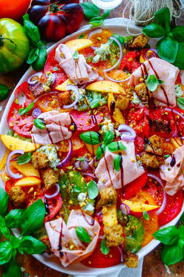 Lekker makkelijk recept voor Tomaten salade met pesto, simpel snelle salade voor bij een BBQ - barbecue of als doordeweekse maaltijd. Fris, licht, zomers en gezond. Dunne plakjes tomaat, perzik, pesto ricotta crème, pesto croutons en mortadella. Heerlijke dagelijkse kost